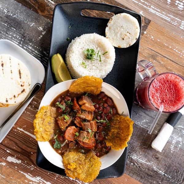 A Colombian Bandeja Paisa with rice, beans, meat, avocado, and plantains, served with a red drink.