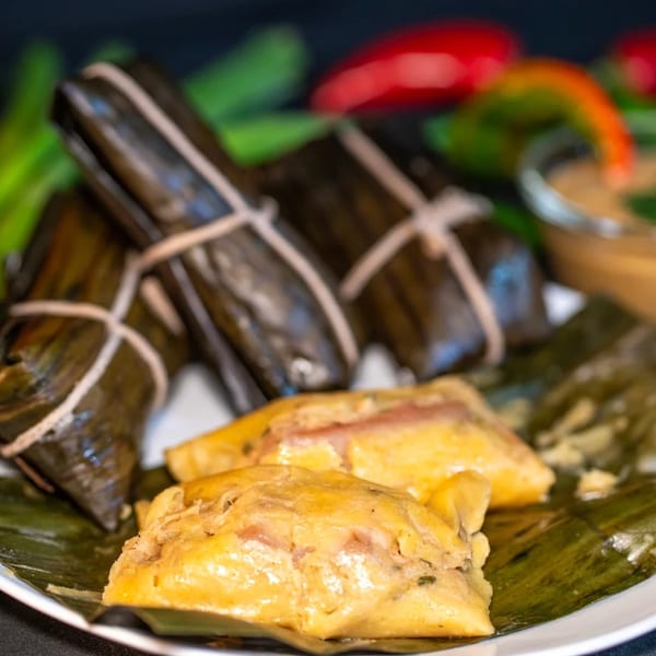Colombian tamales, some wrapped in banana leaves and others unwrapped, on a white plate.