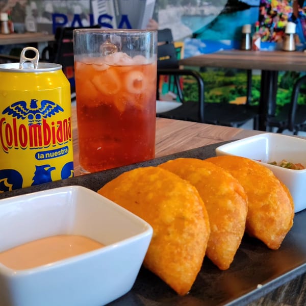 Colombian empanadas with dipping sauces, a glass of iced tea, and a Colombiana soda can.
