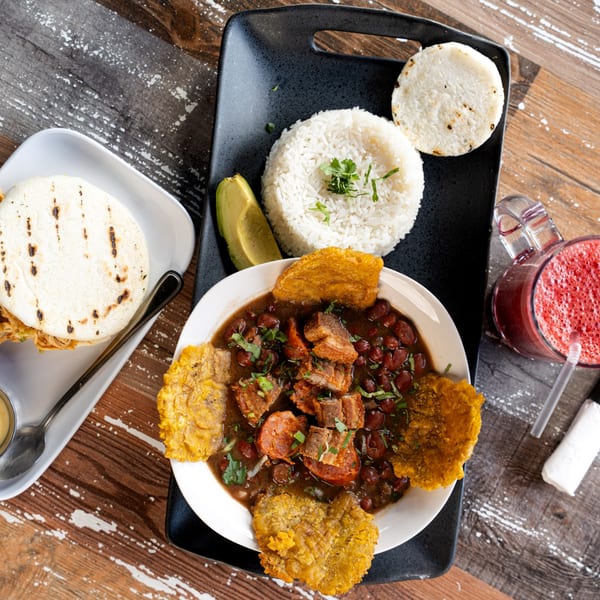 Colombian bandeja paisa with rice, beans, meat, plantains, avocado, and an arepa on a wooden table.