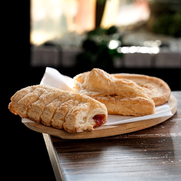 Golden-brown Colombian pastries, one filled with guava, on a wooden tray with white paper.